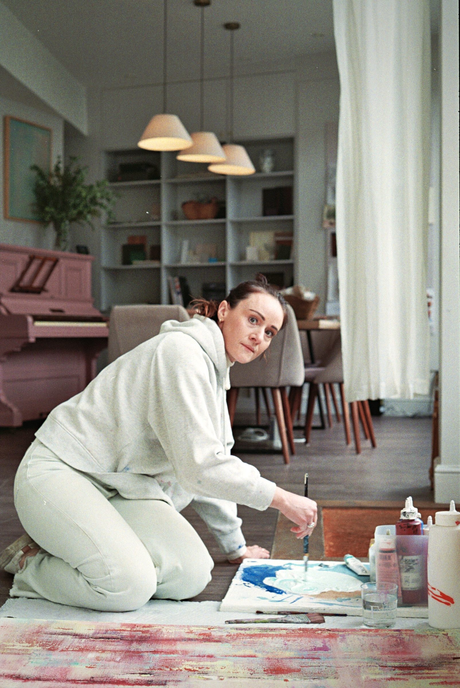 Artist painting on studio floor, looking at camera