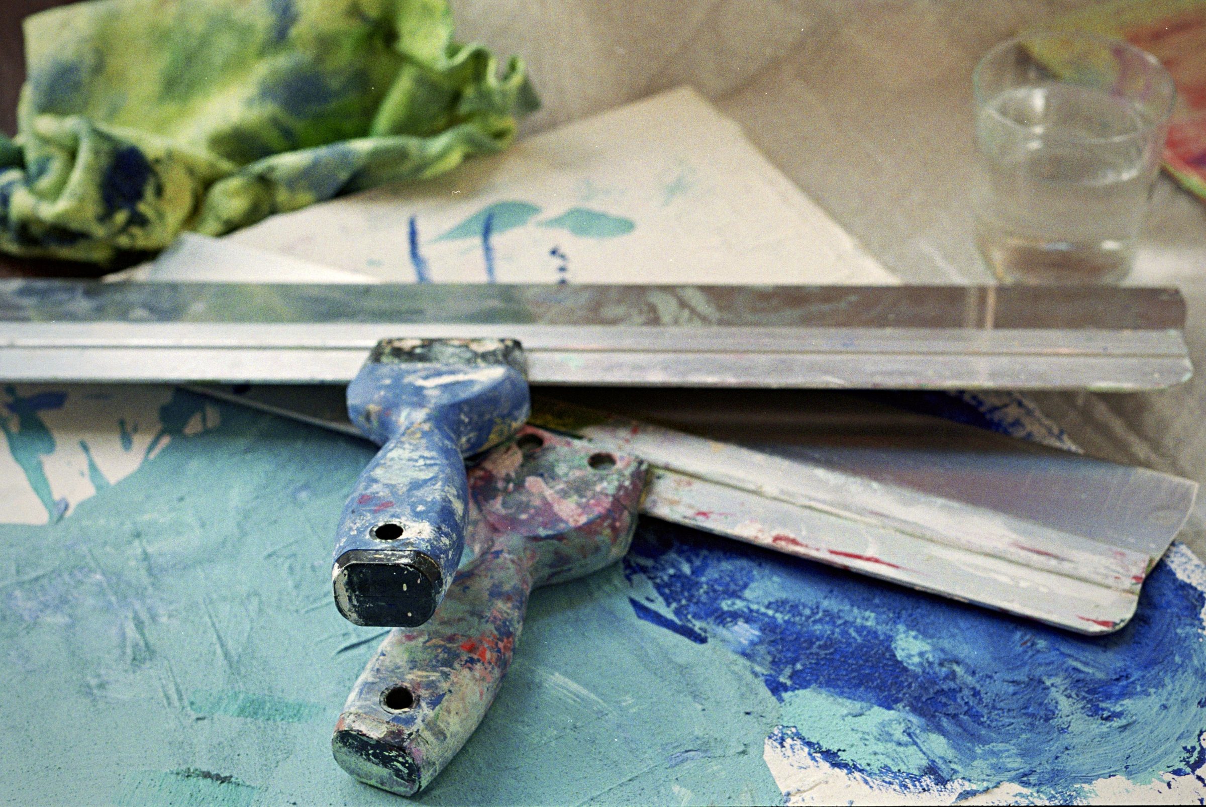 Paint squeegee on teal blue canvas — artist tools