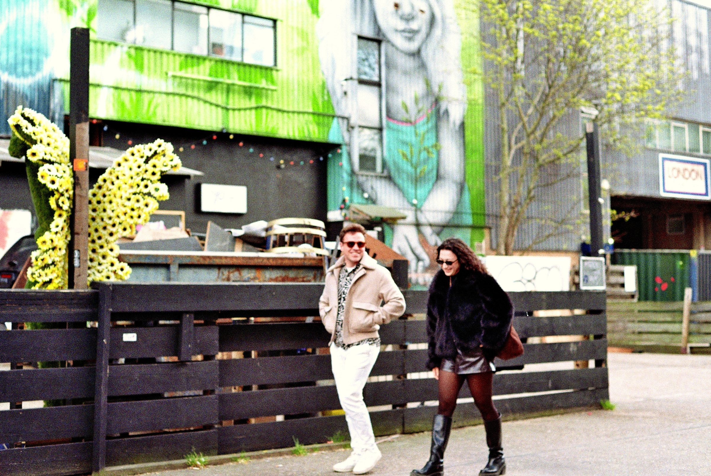 Couple walking past street art mural Hackney London — lifestyle portrait
