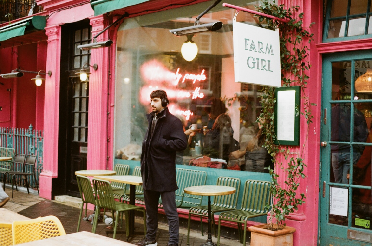 A man in headphones standing outside a bright pink café front in Notting Hill.