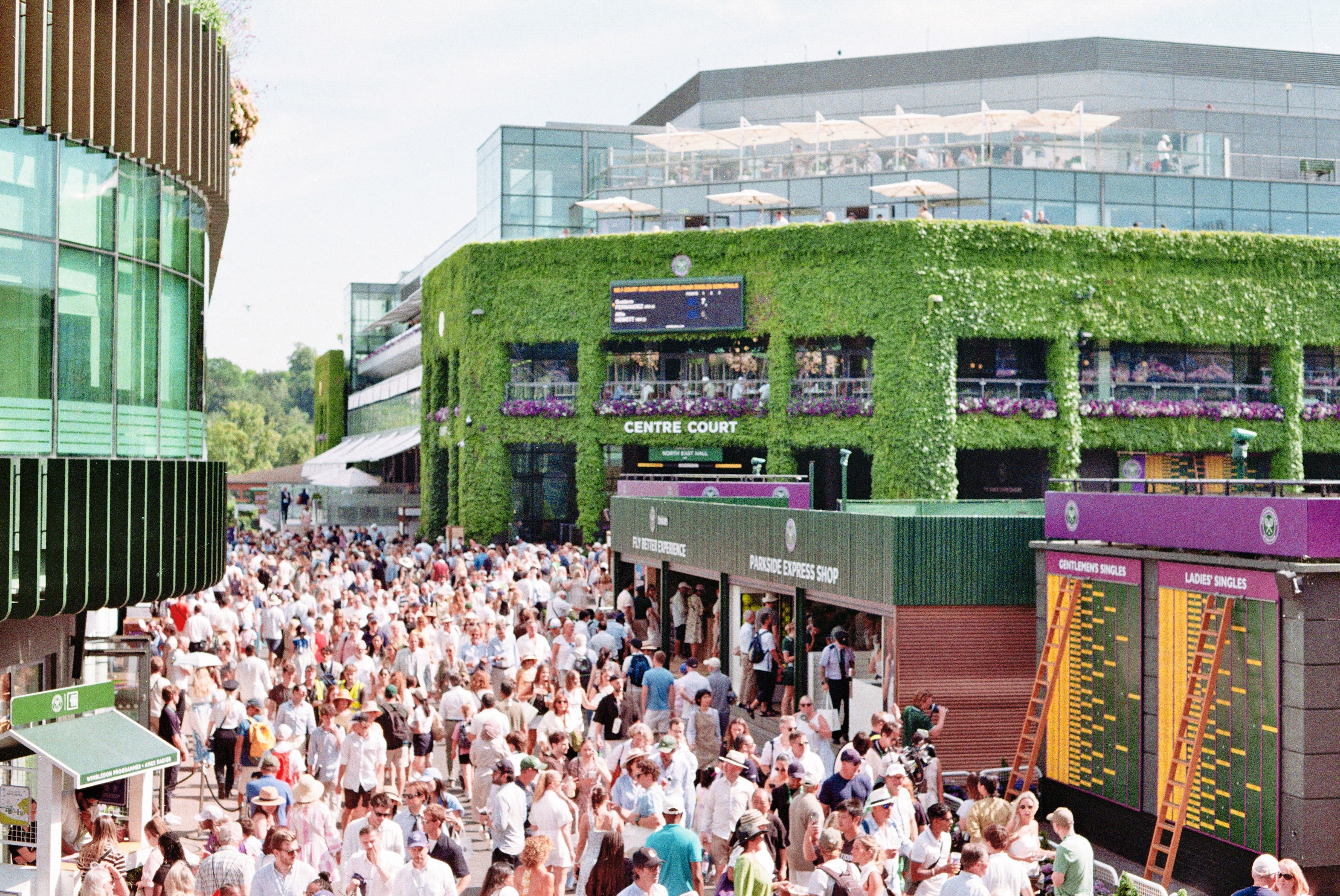 Crowds filling the grounds in front of the ivy-clad Centre Court building on a bright afternoon.