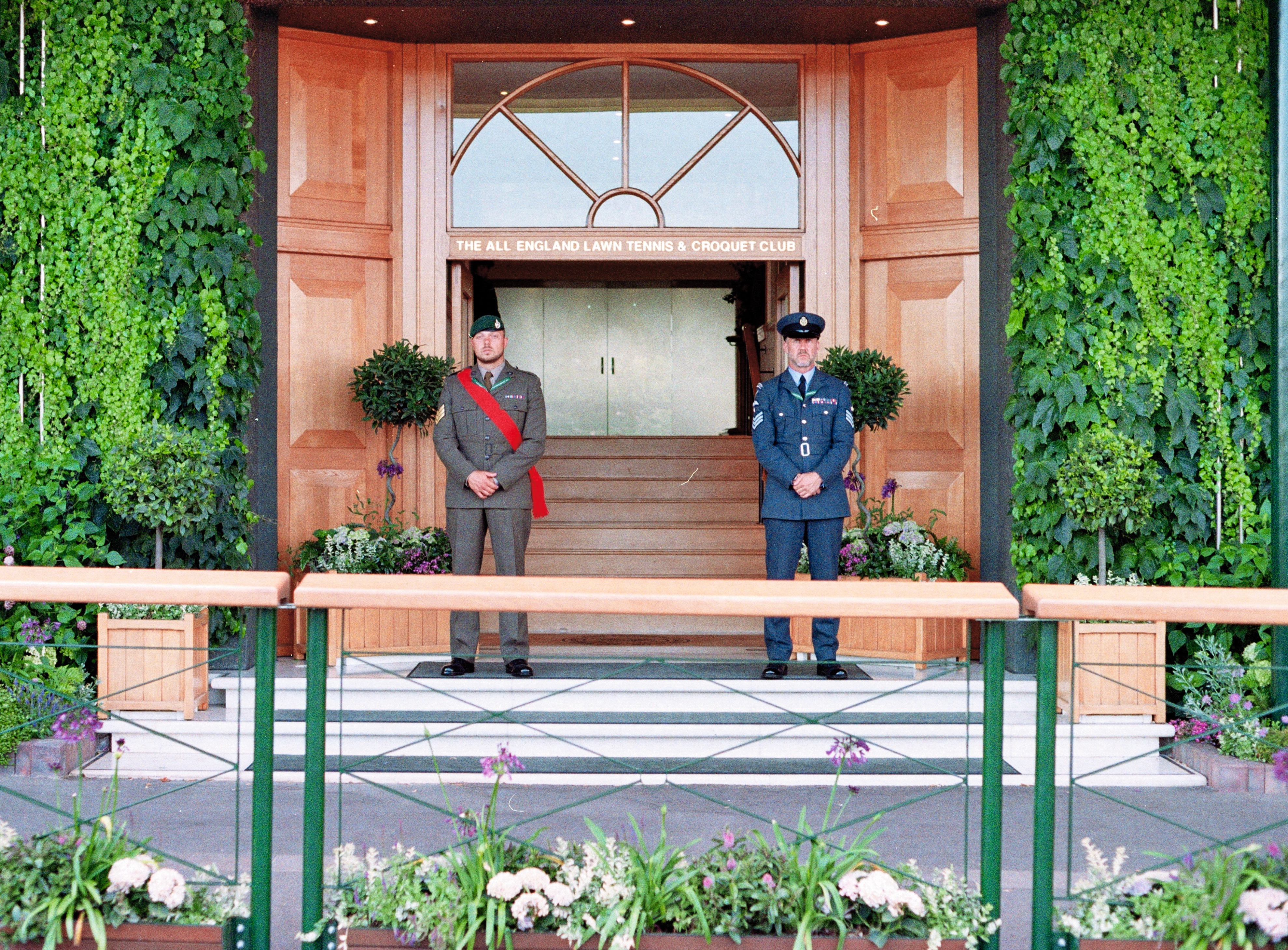Two servicemen in dress uniform standing either side of the ivy-framed clubhouse entrance.