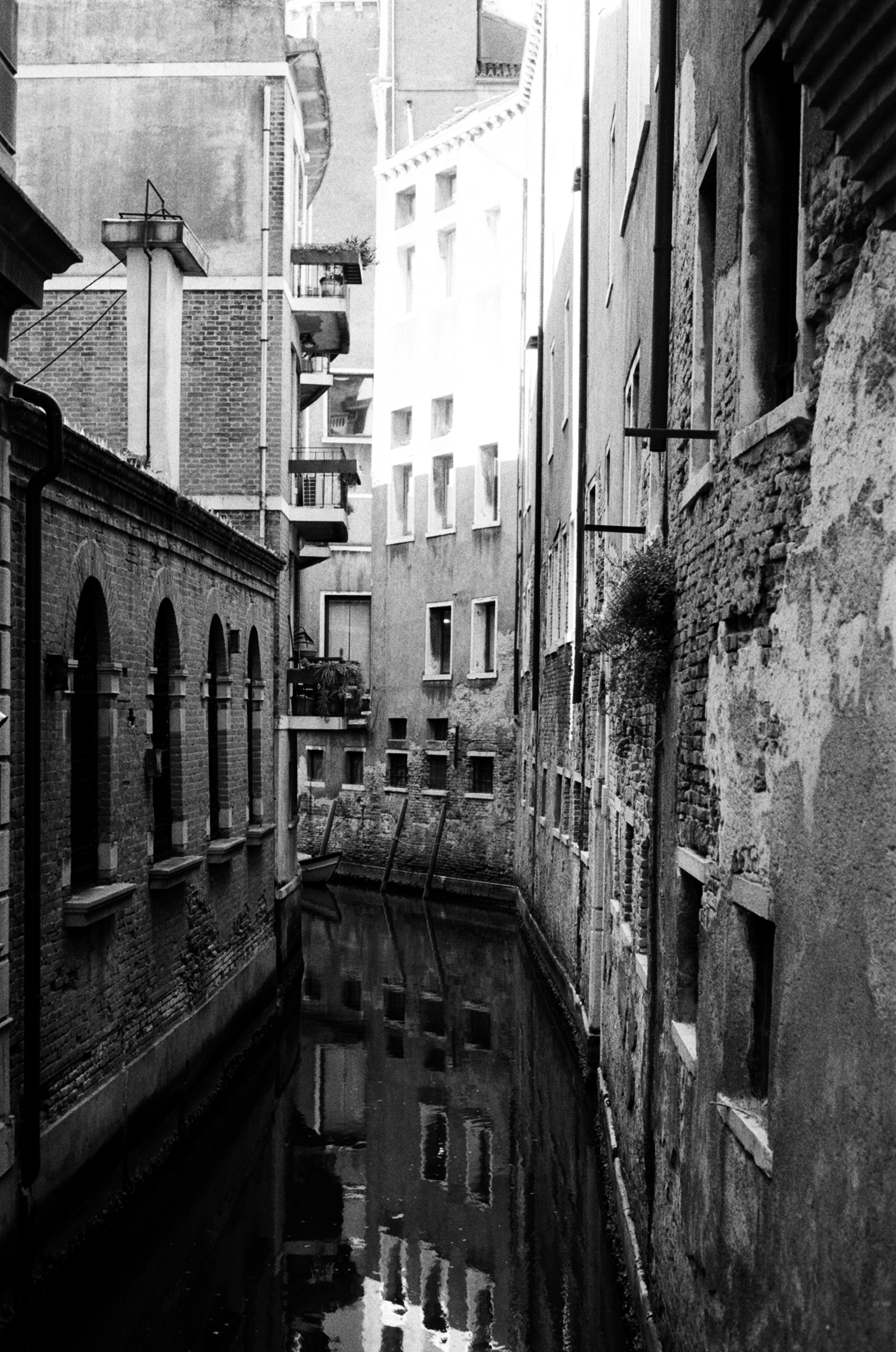 A narrow Venetian canal in deep shadow, arched windows along the left wall, reflections held in still black water.