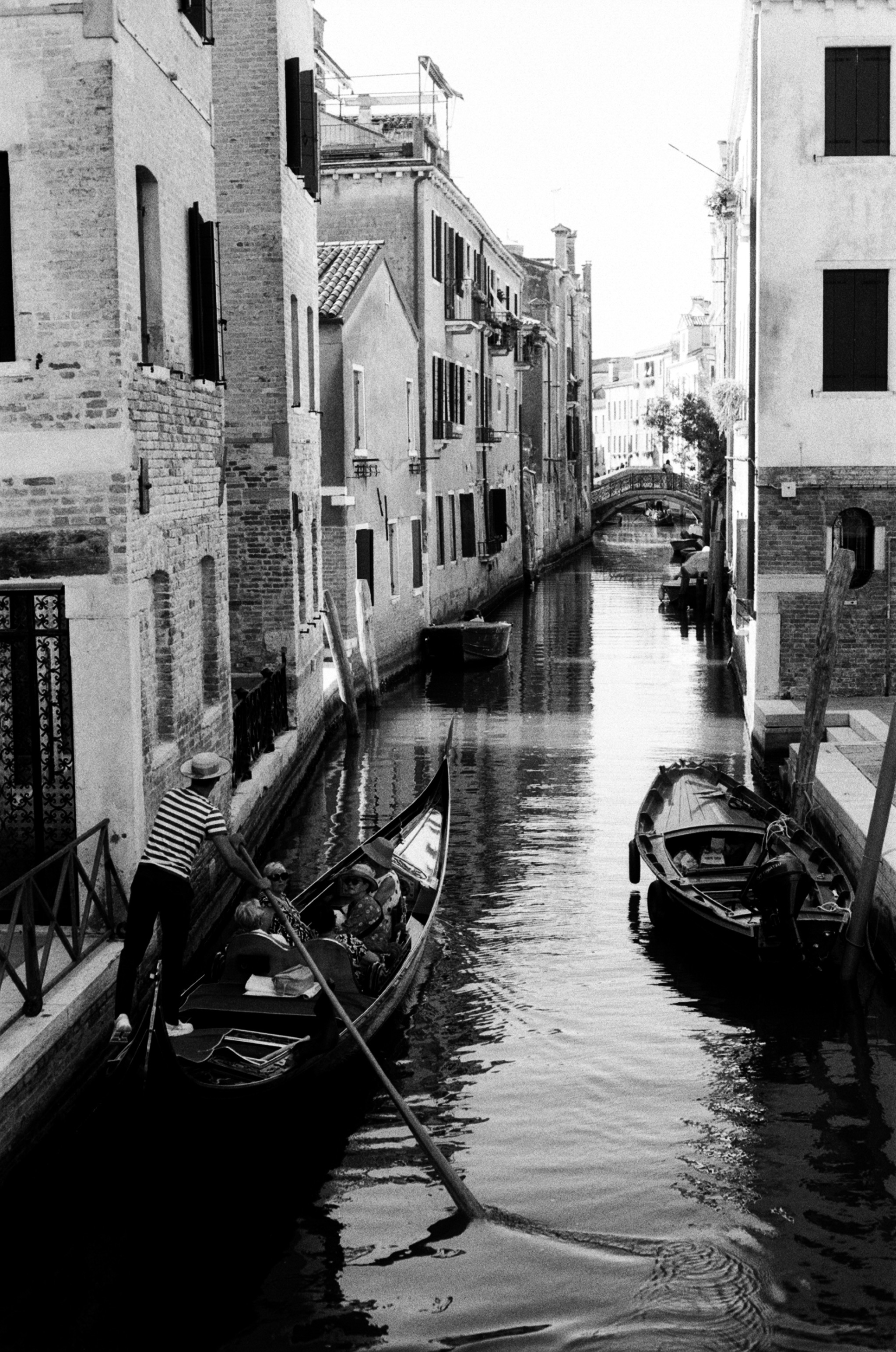 A long canal receding to a footbridge, a gondolier working the oar in the left foreground.