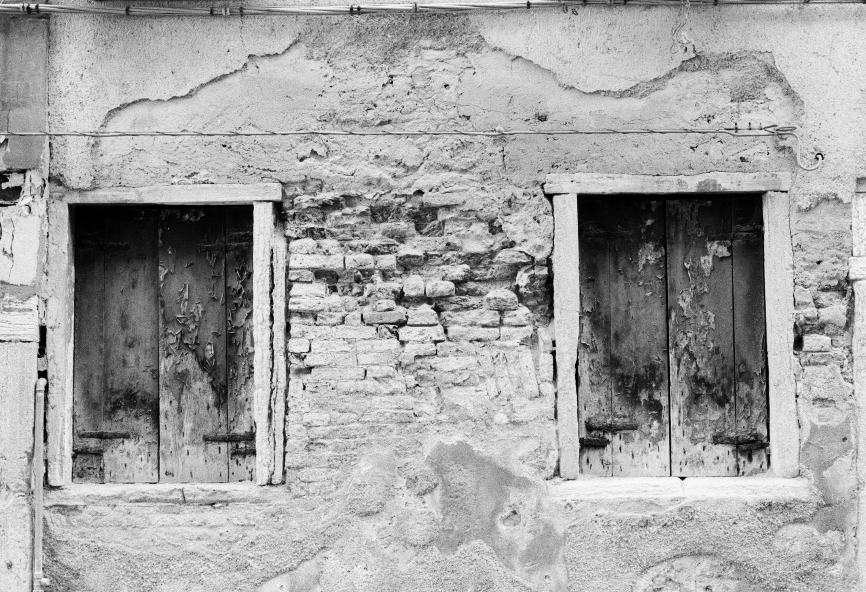 Two weathered wooden shutters set into a wall of crumbling plaster and exposed brick.